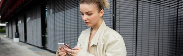 Mulher em casaco de trincheira usando celular na rua urbana, banner — Fotografia de Stock