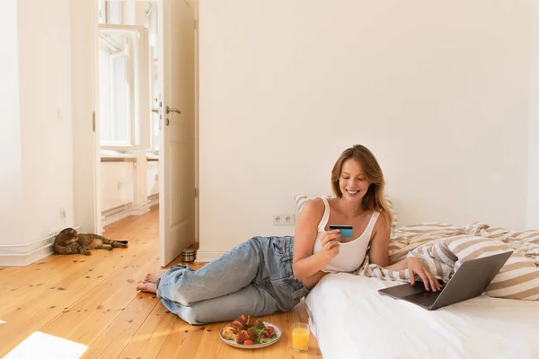 Jeune femme utilisant un ordinateur portable et carte de crédit près du petit déjeuner et chat pliant écossais à la maison — Photo de stock