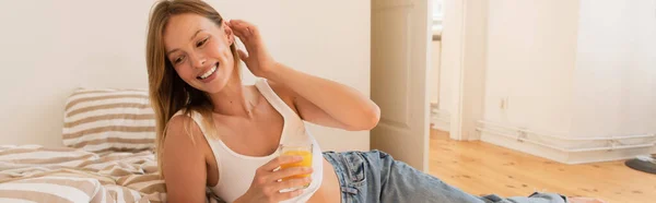 Cheerful young woman holding orange juice near bed at home, banner — Stock Photo
