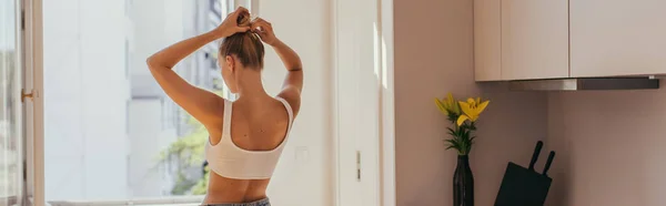 Blonde woman in top touching hair in kitchen, banner — Stock Photo