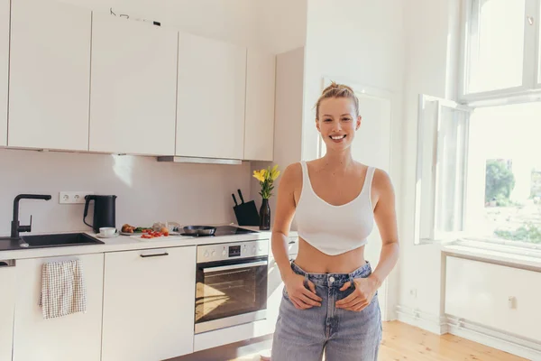 Mujer rubia positiva en la parte superior mirando la cámara en la cocina - foto de stock