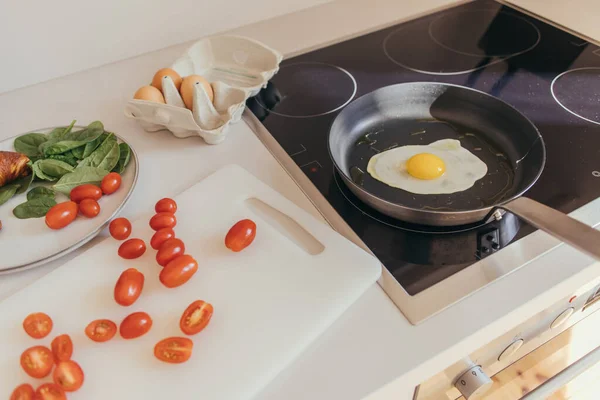 Яйцо на сковороде рядом с помидорами черри и шпинатом на кухне — стоковое фото