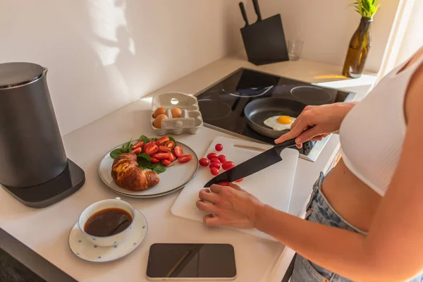 Vista recortada de la mujer cortando tomates cherry cerca de café y teléfono inteligente en casa - foto de stock