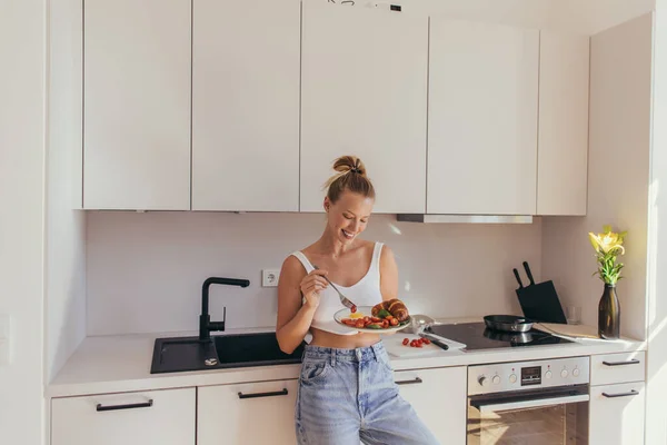 Smiling woman in top holding plate with breakfast in kitchen — Stock Photo