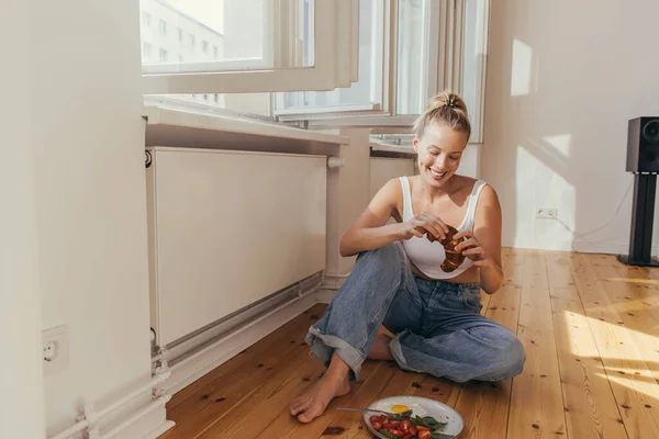 Sorrindo mulher segurando croissant perto do café da manhã no chão em casa — Fotografia de Stock