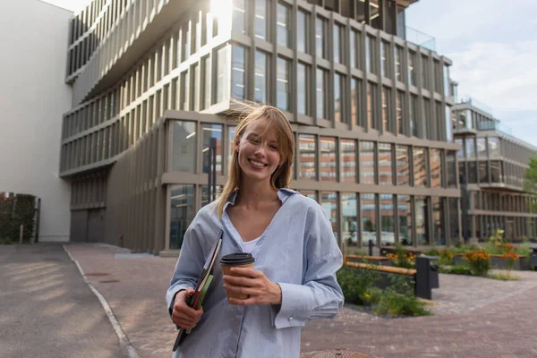 Mulher loira positiva segurando dispositivos e café para ir na rua urbana em Berlim — Fotografia de Stock
