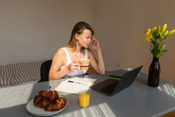 Side view of freelancer holding cup while suffering from headache near devices and breakfast at home — Stock Photo