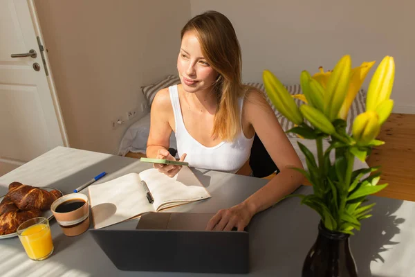 Blonde freelancer using smartphone and laptop near breakfast at home — Stock Photo