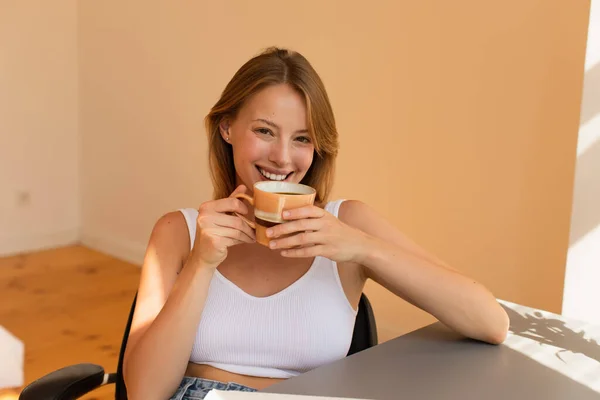 Mujer rubia feliz en la parte superior sosteniendo la taza de café en casa - foto de stock