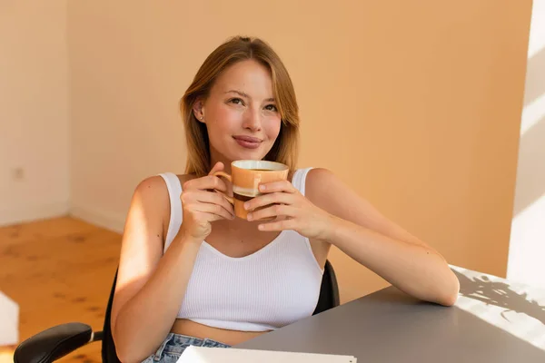 Mulher loira sonhadora no topo segurando xícara de café em casa — Fotografia de Stock