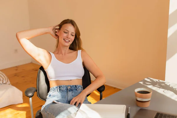 Lächelnde Freiberuflerin sitzt neben Laptop und Kaffee zu Hause — Stockfoto