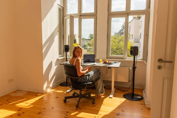 Jovem mulher usando smartphone perto de laptop e café da manhã em casa — Fotografia de Stock