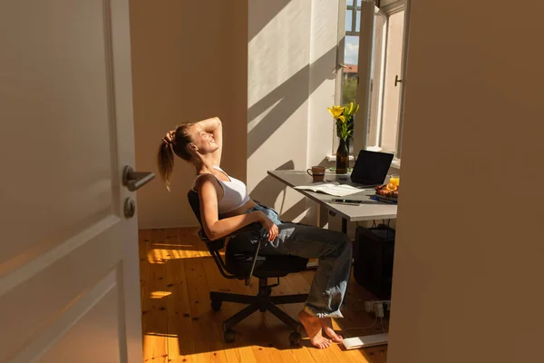 Seitenansicht positiver Freiberufler, der neben Geräten sitzt und zu Hause frühstückt — Stockfoto