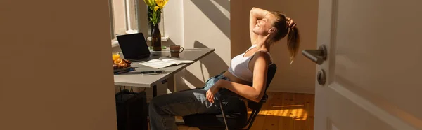 Vista lateral do freelancer alegre sentado perto de gadgets e café da manhã em casa, banner — Fotografia de Stock