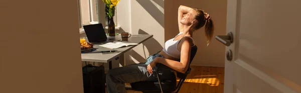 Side view of cheerful freelancer sitting near gadgets and breakfast at home, banner — Stock Photo