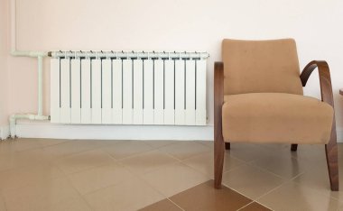 Modern bir alüminyum beyaz ısıtma radyatörü ve yerleşim alanındaki bir duvarın arka planında şık kahverengi bir koltuk..