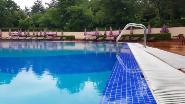 4k-Video, frühmorgens auf dem Gelände eines Freibades, im Hintergrund wischt eine Reinigungskraft mit einem Wischmopp den Boden, ein leerer Luxus-Pool — Stockvideo