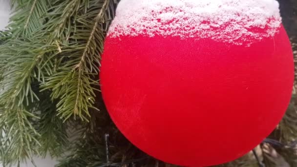 4k video, close-up of red and gold balls on a Christmas tree, covered with snow, outdoors. Background of Christmas tree decorations and garlands