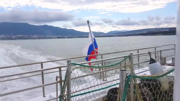 Gemideki Rus bayrağı, rüzgarda dalgalanıyor, Karadeniz 'in arka planına ve Gelendzhik manzaralı kıyı şeridine yakın plan. — Stok video