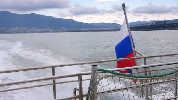 Gemideki Rus bayrağı, rüzgarda dalgalanıyor, Karadeniz 'in arka planına ve Gelendzhik manzaralı kıyı şeridine yakın plan. — Stok video