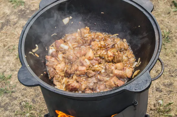 オープン火災でストーブの上に大きなフライパンで揚げ肉を調理 屋外の家族の夕食 クローズアップ — ストック写真