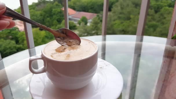 4K视频 一杯热咖啡 一个女人的手搅动着一杯上有勺子的美味卡布奇诺 在阳台上的玻璃桌上小酌一口 — 图库视频影像