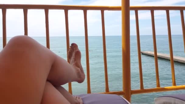 4K视频 一个年轻女子躺在海边和日光浴的躺椅上的观点 暑假期间 在海滩上 女人在躺椅上的腿放松一下 享受一下 — 图库视频影像