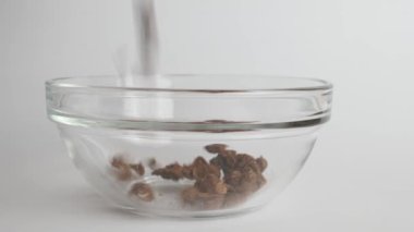 Granola is poured into a transparent bowl on a white background. Healthy food.