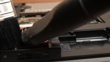 The wizard cleans the laptop's cooling system with a brush and a vacuum cleaner. PC care and repair concept.