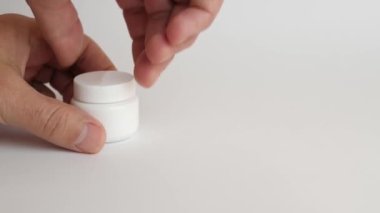 The man opens a plastic bottle and pours medical capsules on his arm. Use of medical devices.
