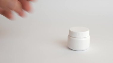 The man opens a plastic bottle and pours medical capsules on his arm. Use of medical devices.