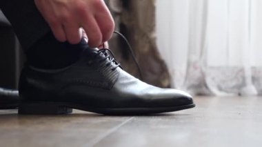 The man puts on new leather shoes and ties the laces.