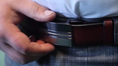 Deri kemeri metal bir tokayla düzeltip sıkıyor..