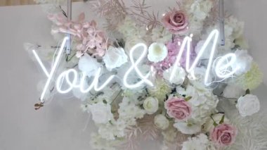 The inscription You & Me in the form of light bulbs under the glass on a background of flowers.