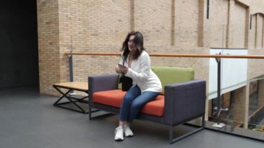 Güzel bir kız alışveriş merkezinde oturuyor ve akıllı bir telefonla konuşuyor..