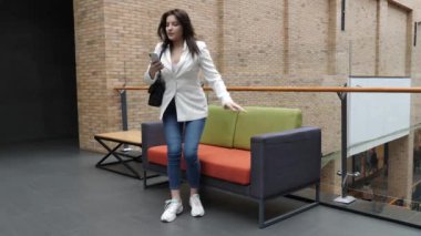 Güzel bir kız alışveriş merkezinde oturuyor ve akıllı bir telefonla konuşuyor..