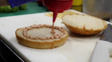 Hamburger yapmak için sosu ekmeğin üzerine sürüyorum.
