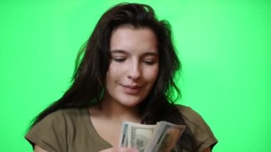 Güzel genç kız yeşil arka planda dolarları sayıyor..
