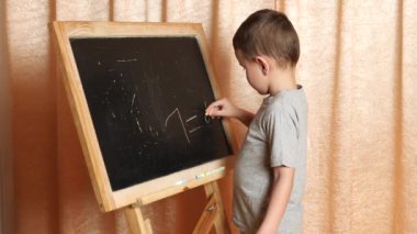 Evde öğreniyorum. Çocuk tahtaya tebeşirle yazmayı öğreniyor..