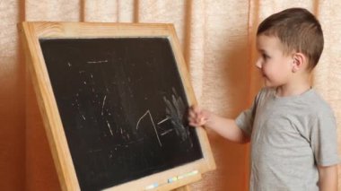 Evde öğreniyorum. Çocuk tahtaya tebeşirle yazmayı öğreniyor..