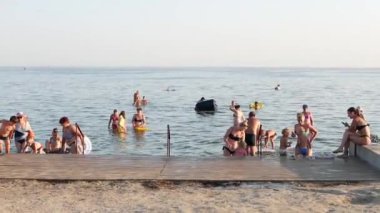 Akşam denizi. İnsanlar kumsalda güneşlenir ve banyo yapar..