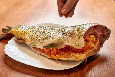 Kadın fırında balık pişirirken baharat ekliyor. Deniz ürünleri pişiriyorum..