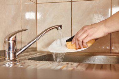 Kadın mutfak lavabosunda bulaşık yıkıyor.