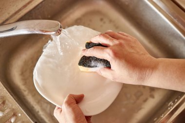 Kadın mutfak lavabosunda bulaşık yıkıyor.
