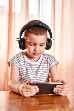 Kulaklıklı küçük çocuk akıllı telefon kullanıyor. 