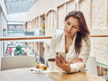 Kafedeki masada otururken cep telefonu kullanan genç bir kadın.