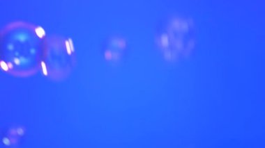Farklı boyutlarda sabun köpükleri mavi arka planda uçar..