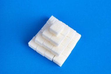 Mavi zemin üzerinde bir piramide istiflenmiş basınçlı şeker küpleri.