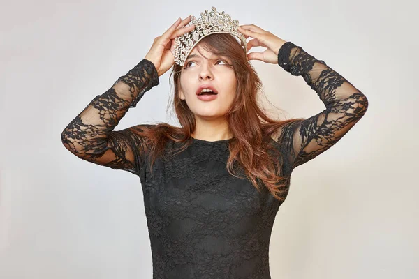 Beautiful upset girl in a black dress with a crown on her head. Beauty contest concept. Emotions of the winner.