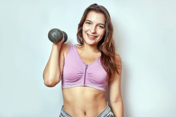 A beautiful girl is standing and trying to lift a heavy dumbbell. Fitness classes.